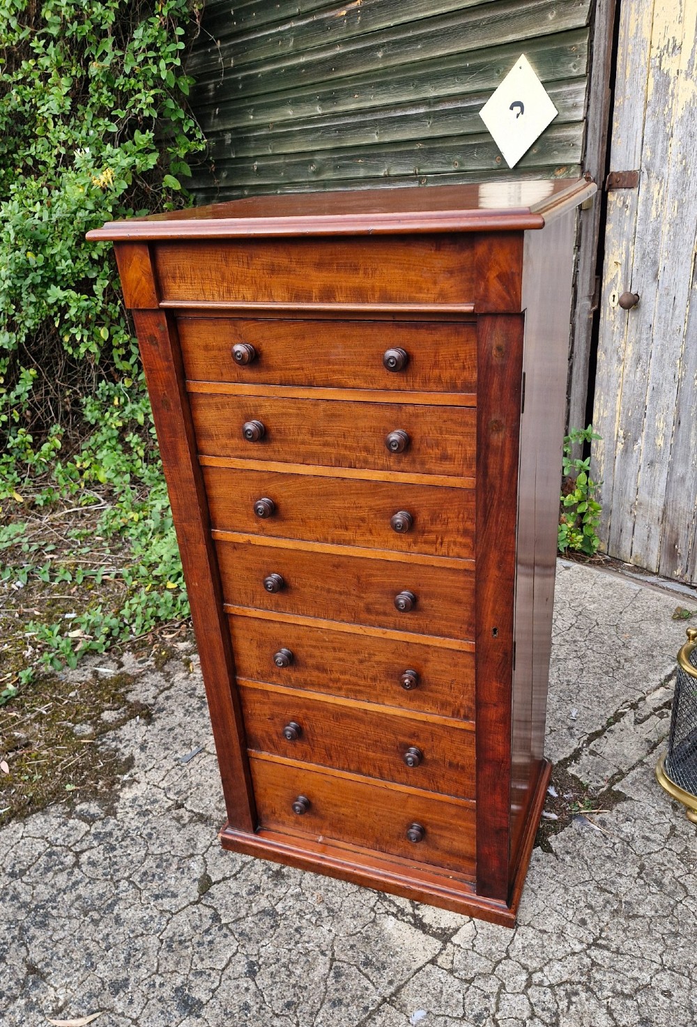 A tall Victorian mahogany Wellington chest featuring seven graduated drawers, turned wooden handles, and a hinged side locking flap. View IV