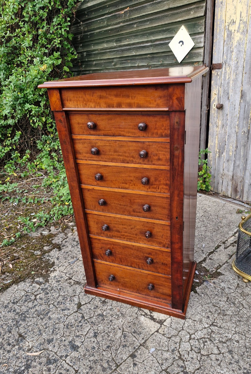 A tall Victorian mahogany Wellington chest featuring seven graduated drawers, turned wooden handles, and a hinged side locking flap. View V