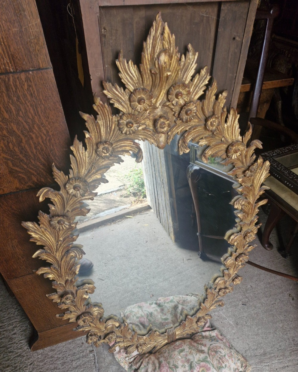An oval wall mirror featuring a carved giltwood frame decorated with detailed acanthus leaves and floral motifs. View III