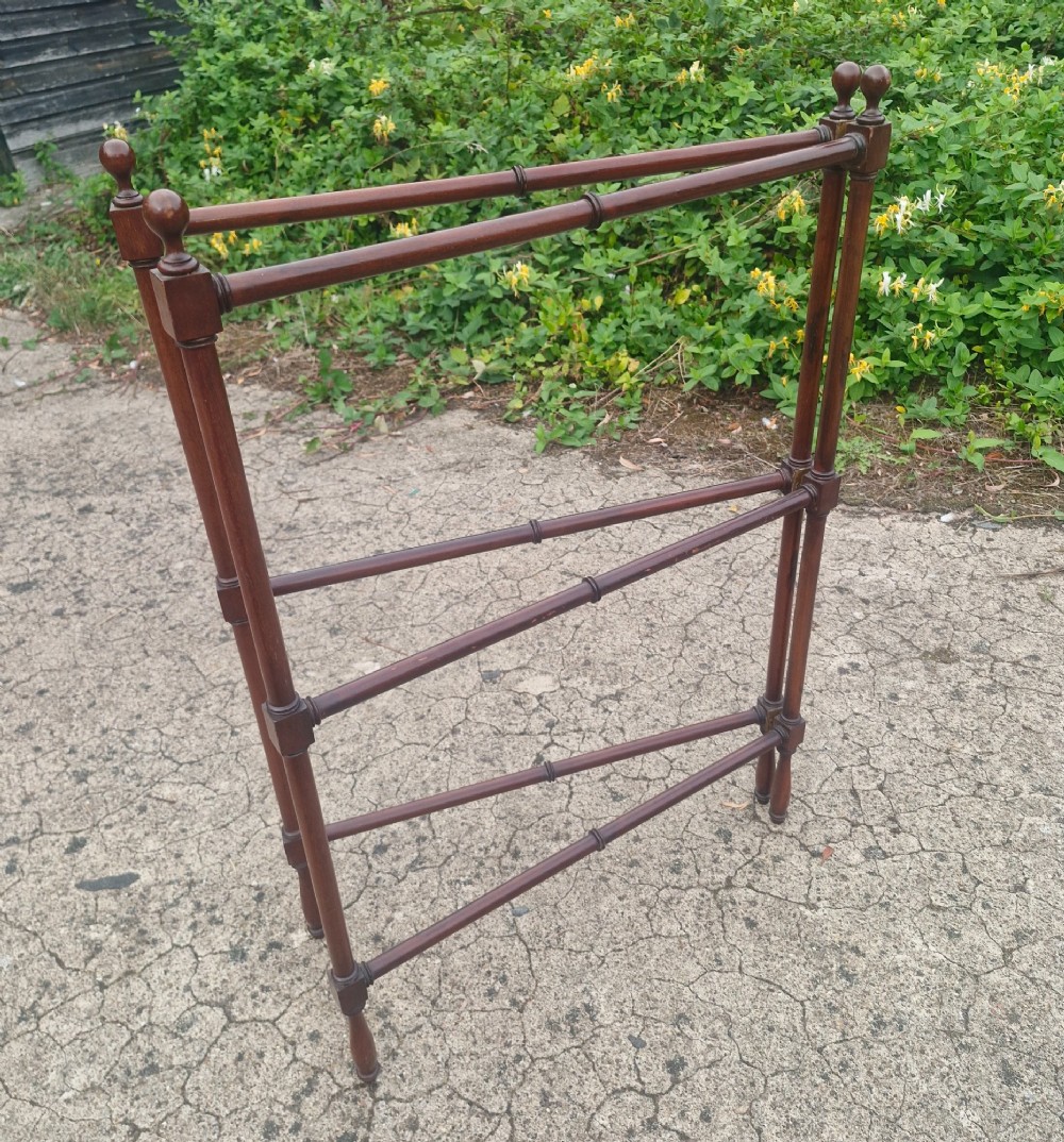 A freestanding mahogany folding towel rail with turned wooden finials and multiple horizontal crossbars on hinged upright supports.
