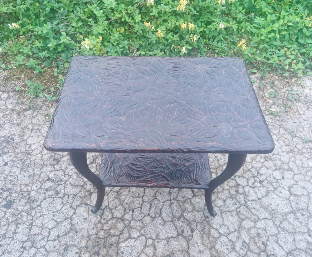 A dark brown two-tier wooden occasional table featuring intricate floral relief carvings across both flat surfaces and supported by four curved legs. View II