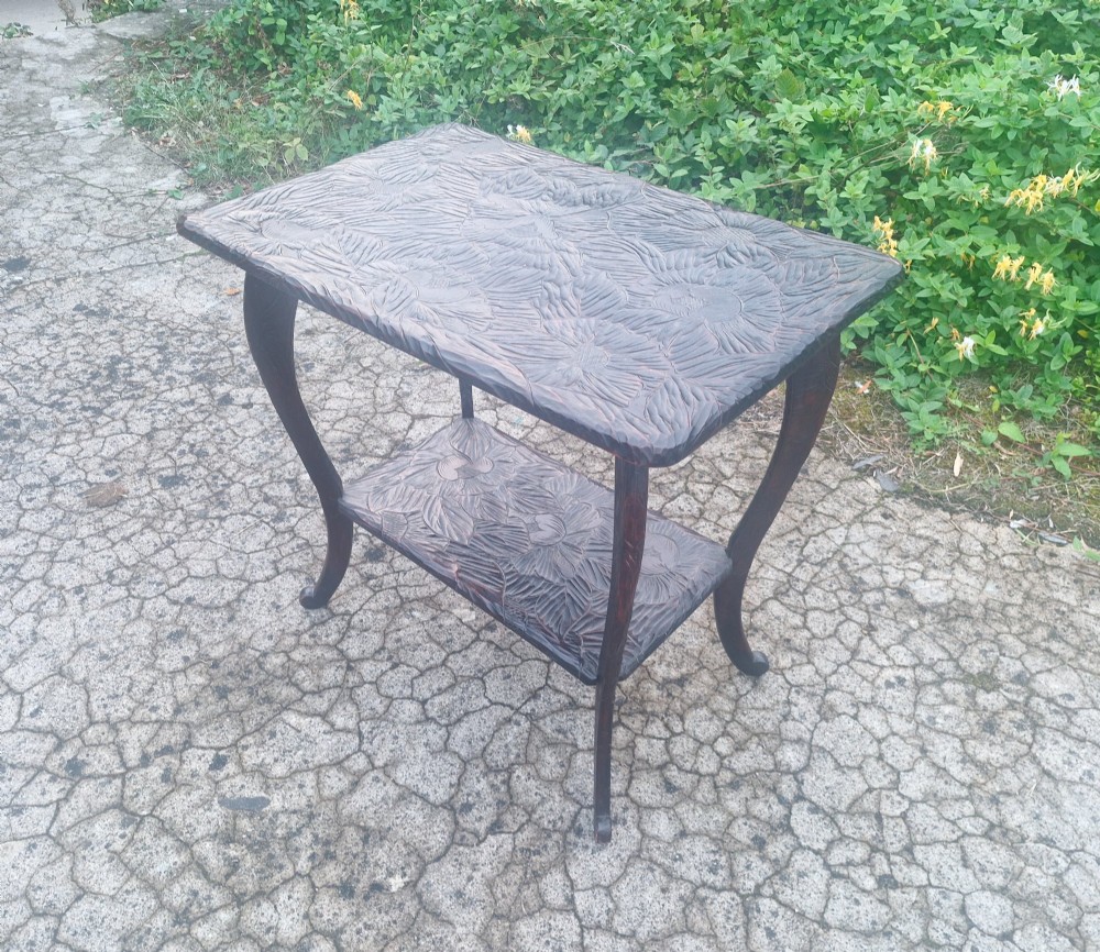 A dark brown two-tier wooden occasional table featuring intricate floral relief carvings across both flat surfaces and supported by four curved legs. View IV