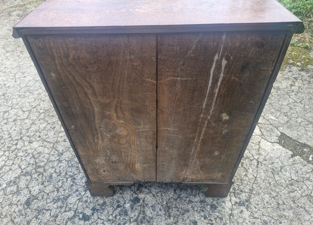 A Georgian oak chest of drawers featuring five graduated drawers with brass swan-neck handles and bracket feet. View II