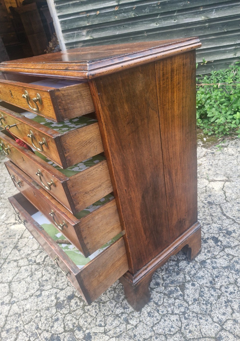 A Georgian oak chest of drawers featuring five graduated drawers with brass swan-neck handles and bracket feet. View III