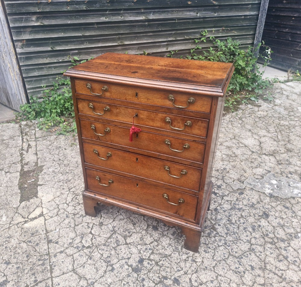 A Georgian oak chest of drawers featuring five graduated drawers with brass swan-neck handles and bracket feet. View VI