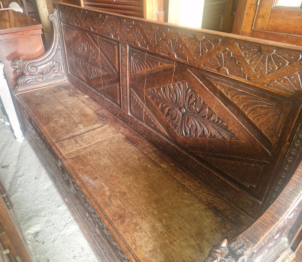 A large Victorian carved dark oak hall bench featuring a high panelled backrest with relief carving and carved lion mask armrests. View III
