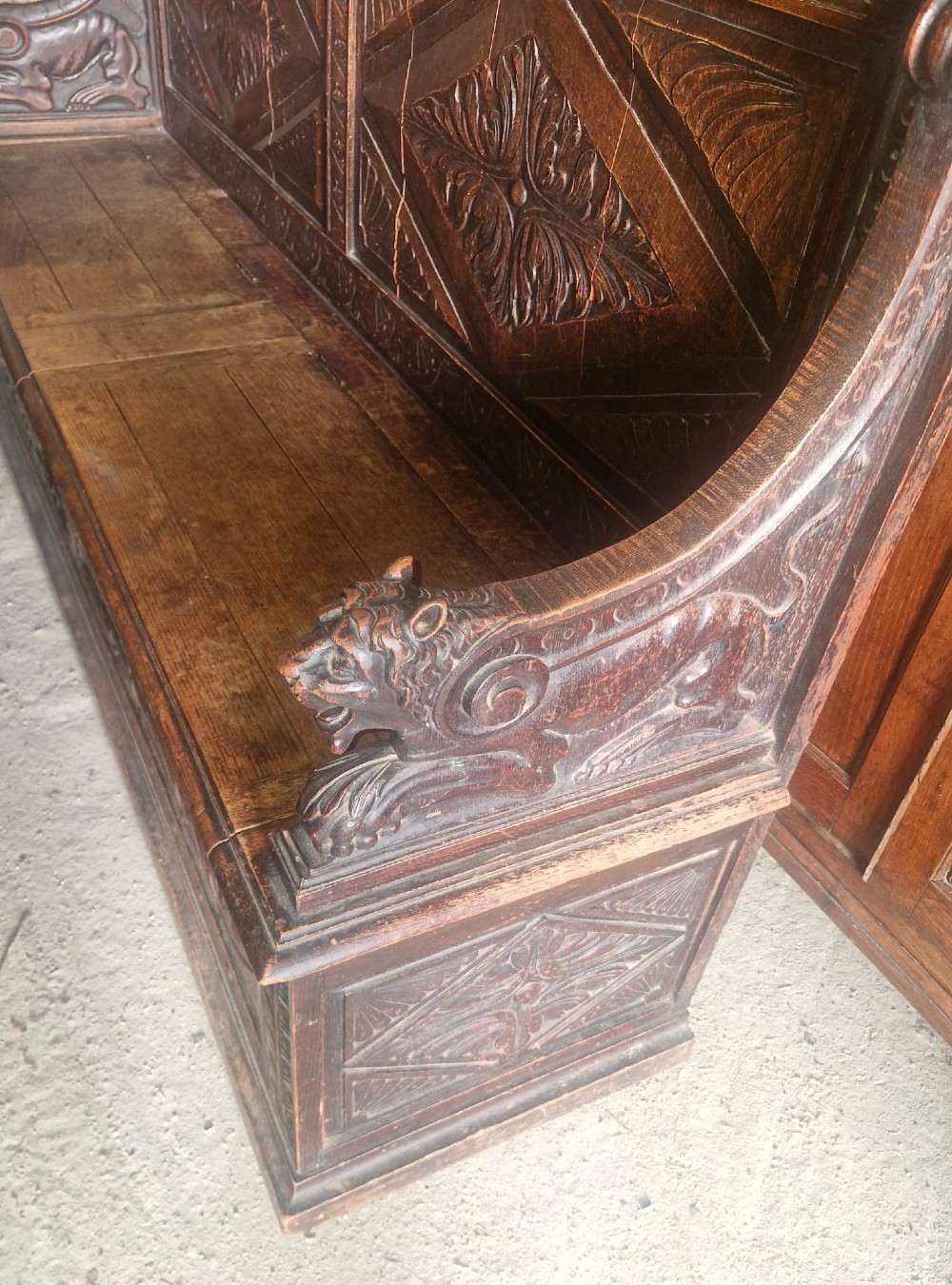 A large Victorian carved dark oak hall bench featuring a high panelled backrest with relief carving and carved lion mask armrests. View IV