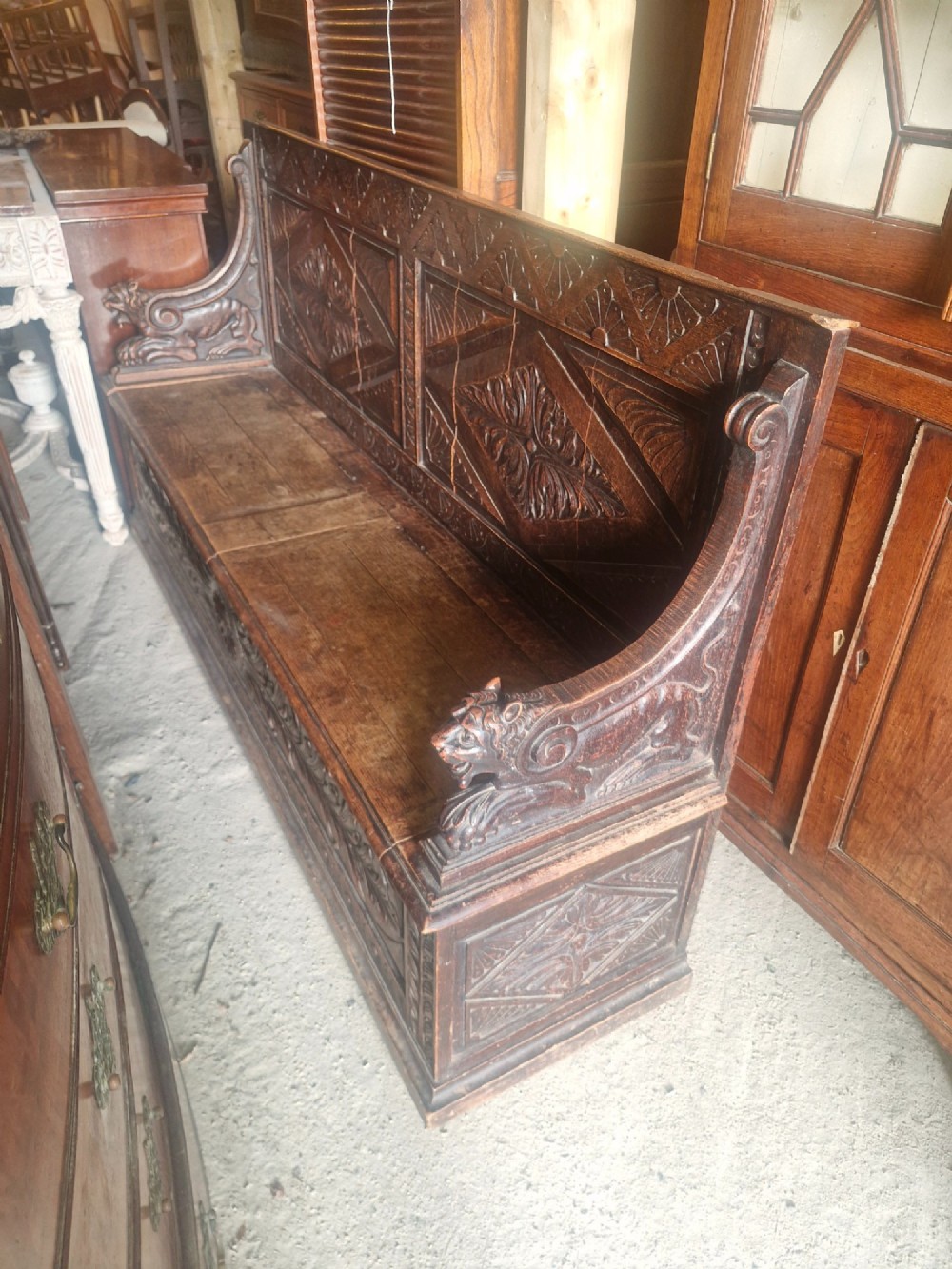 A large Victorian carved dark oak hall bench featuring a high panelled backrest with relief carving and carved lion mask armrests. View V