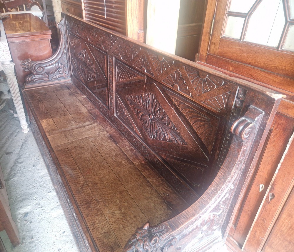 A large Victorian carved dark oak hall bench featuring a high panelled backrest with relief carving and carved lion mask armrests. View VI