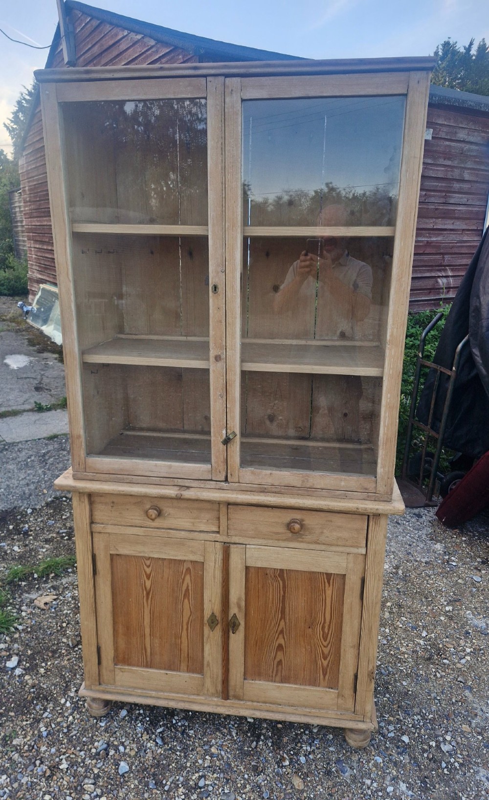 An antique two-part pine kitchen cupboard featuring an upper glazed cabinet with two shelves and a lower base with two drawers above panelled doors.