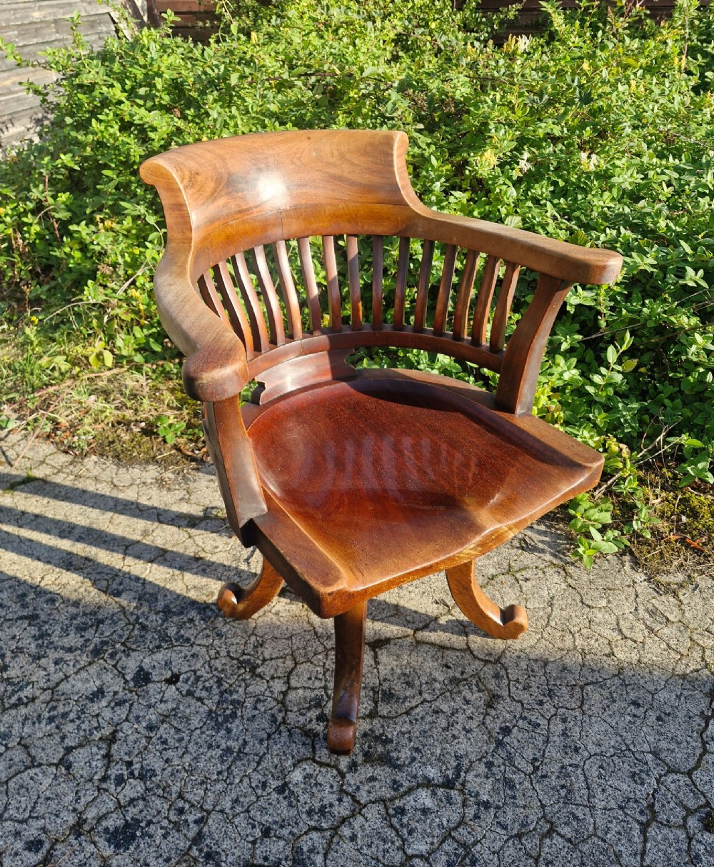 A solid mahogany revolving desk armchair featuring a curved spindle backrest, shaped seat, and splayed legs.