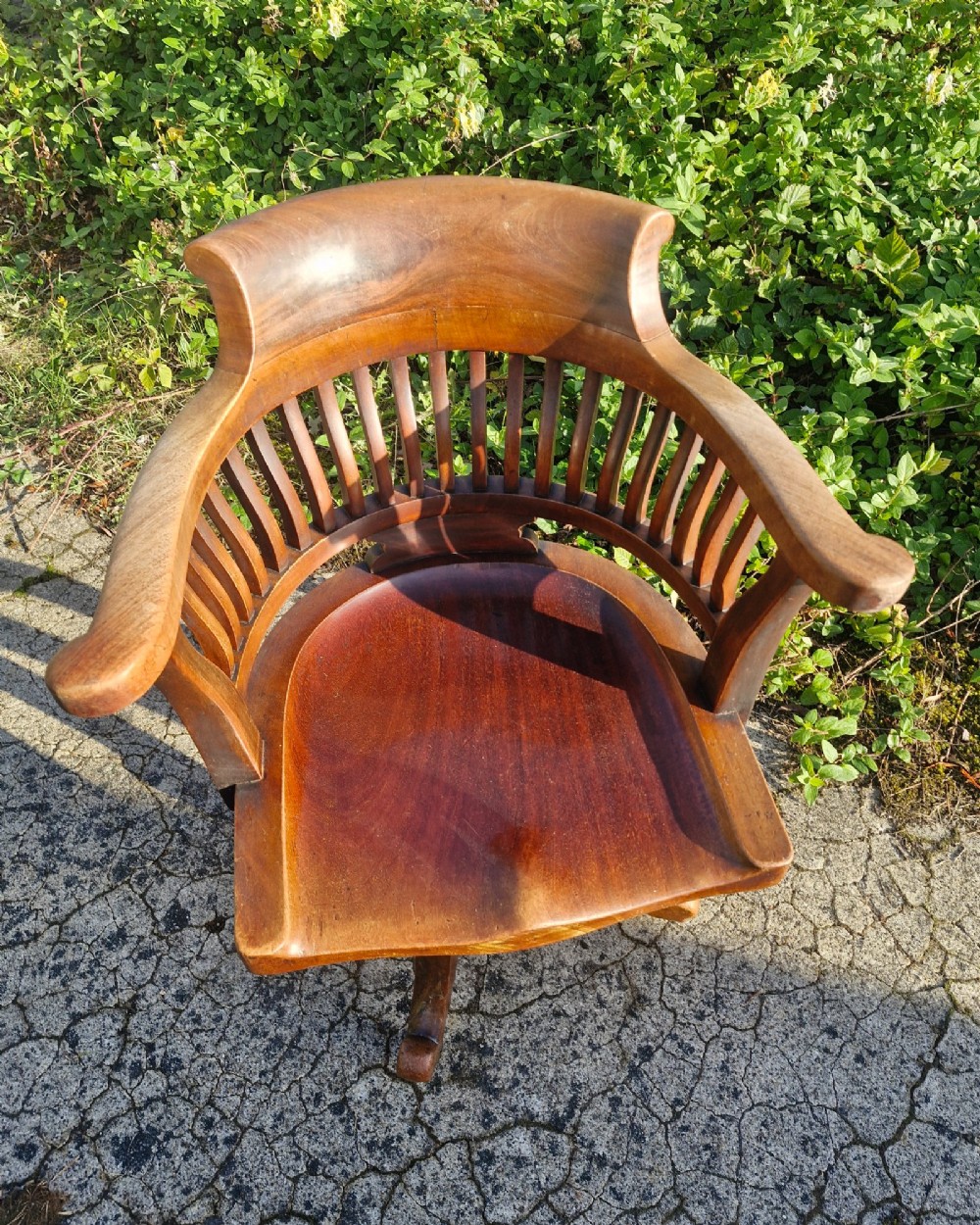 A solid mahogany revolving desk armchair featuring a curved spindle backrest, shaped seat, and splayed legs. View V