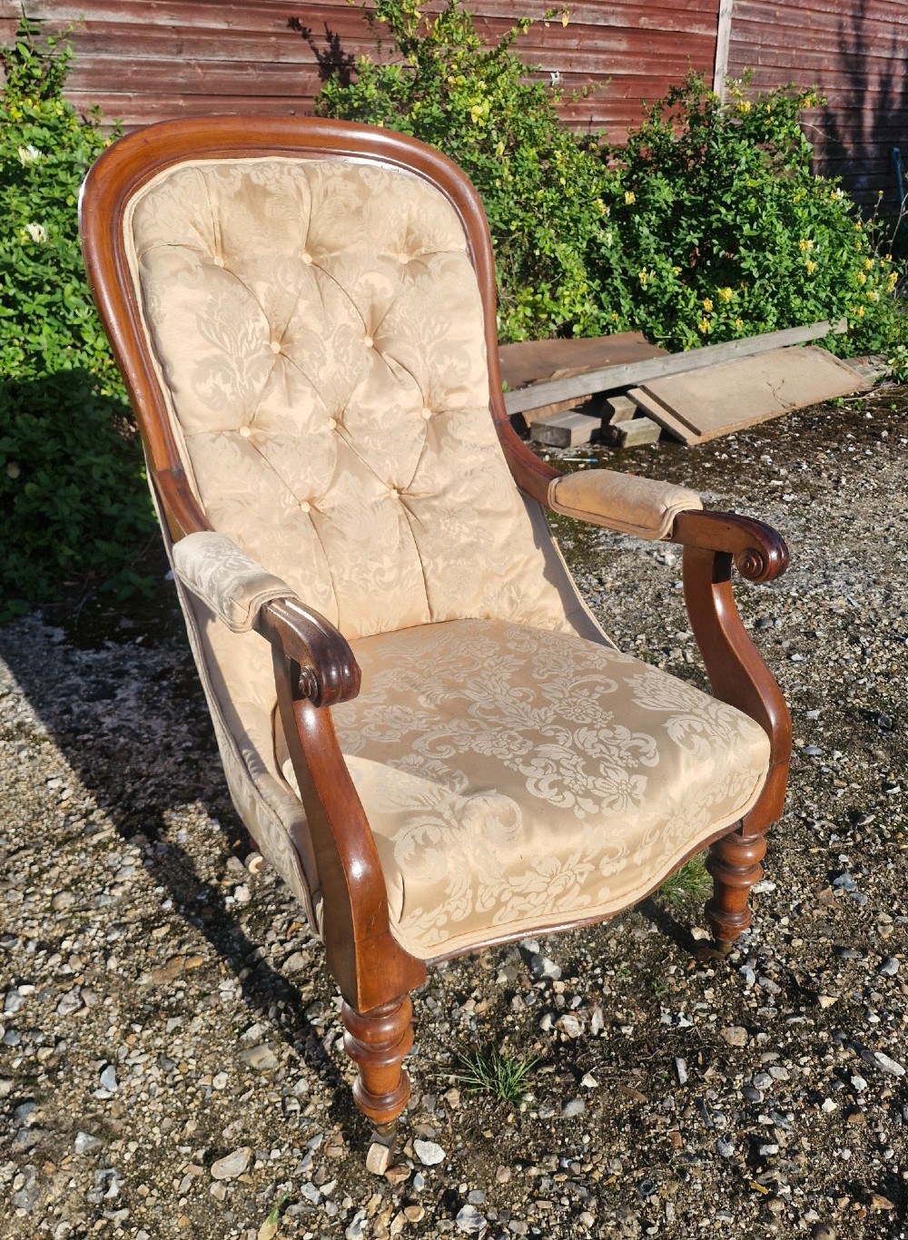 Victorian mahogany library armchair upholstered in gold damask fabric featuring a button-tufted back, scrolled armrests, and turned legs with brass castors. View II