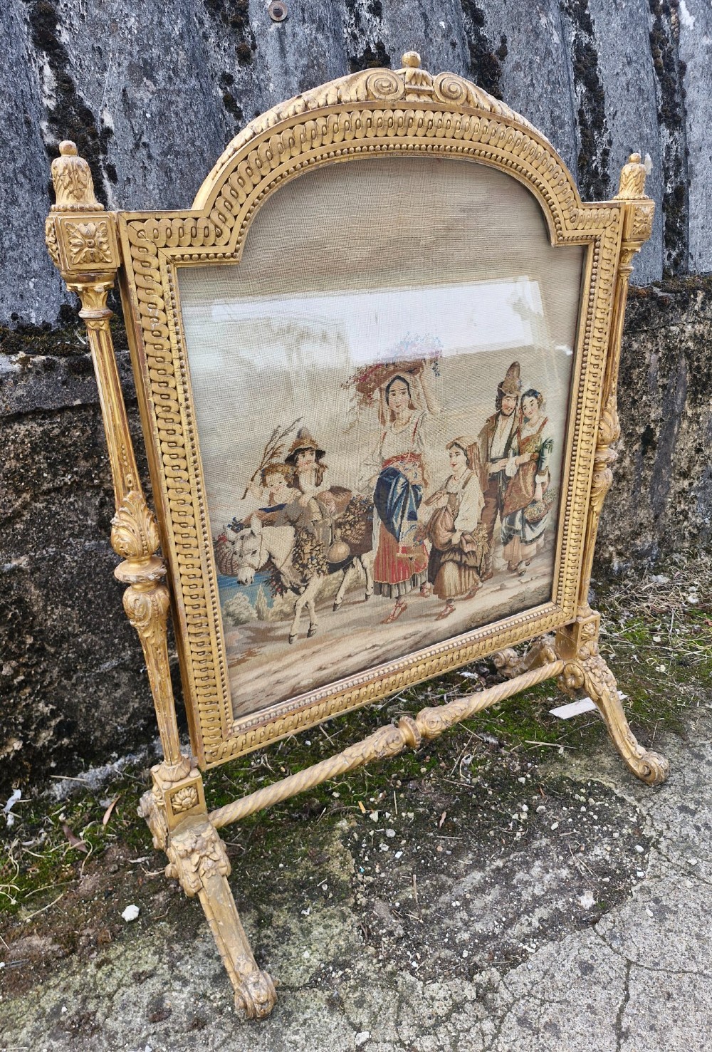 A Victorian carved giltwood fire screen featuring an arched frame, turned side columns, scroll feet, and a central tapestry panel depicting figures in traditional rural attire. View III
