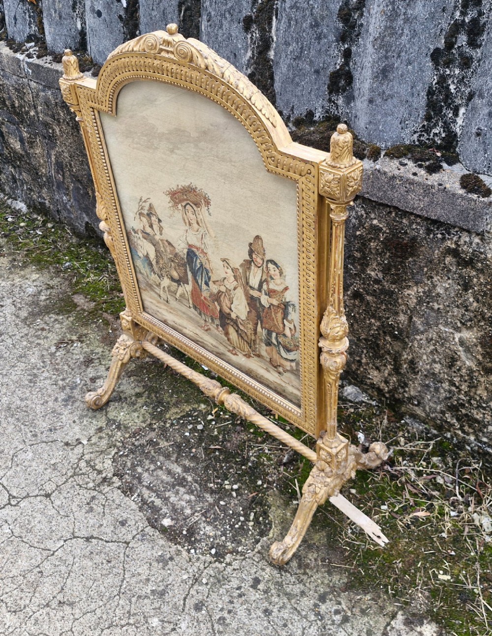 A Victorian carved giltwood fire screen featuring an arched frame, turned side columns, scroll feet, and a central tapestry panel depicting figures in traditional rural attire. View V