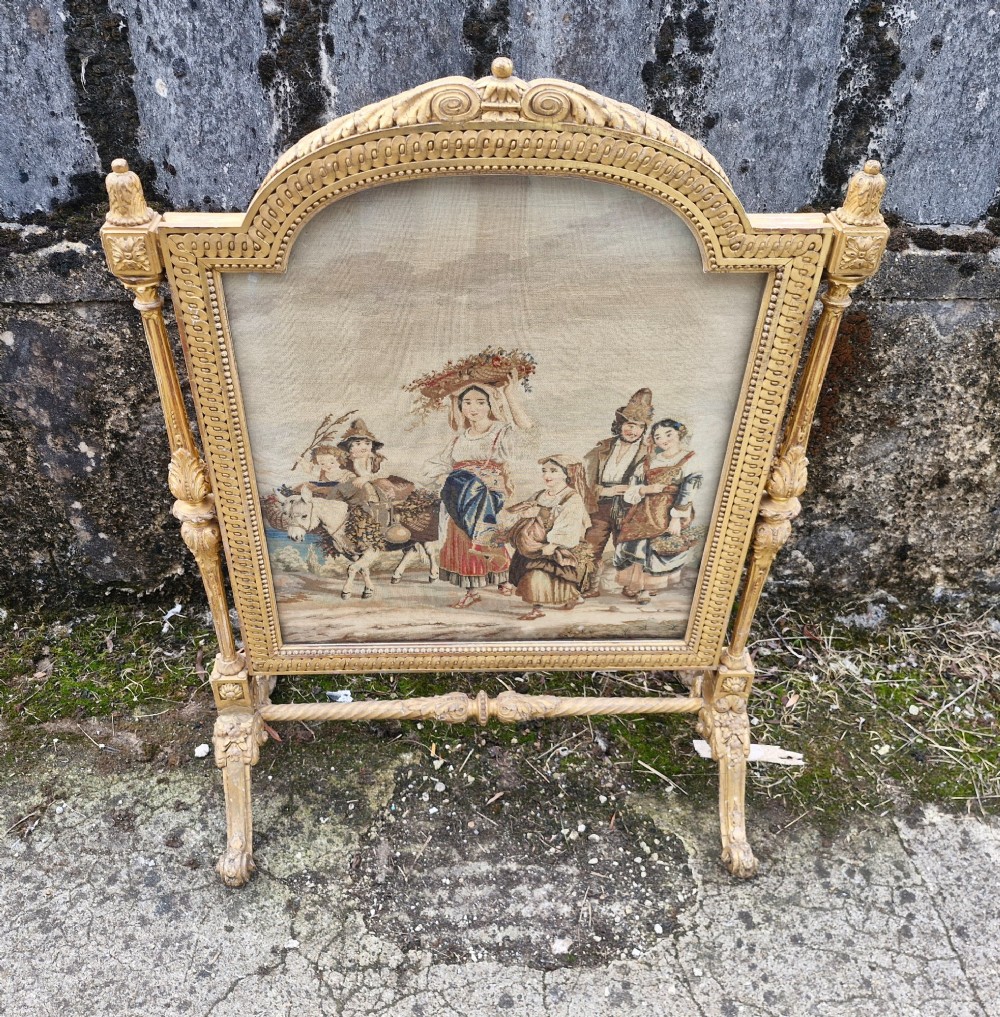 A Victorian carved giltwood fire screen featuring an arched frame, turned side columns, scroll feet, and a central tapestry panel depicting figures in traditional rural attire. View VII