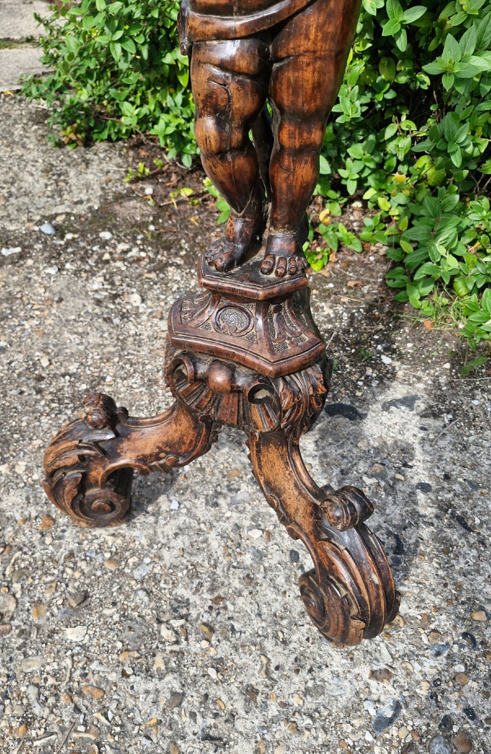 A 19th-century Italian dark carved wood pedestal stand with a putto figure support, scalloped top, and scroll tripod feet. View II