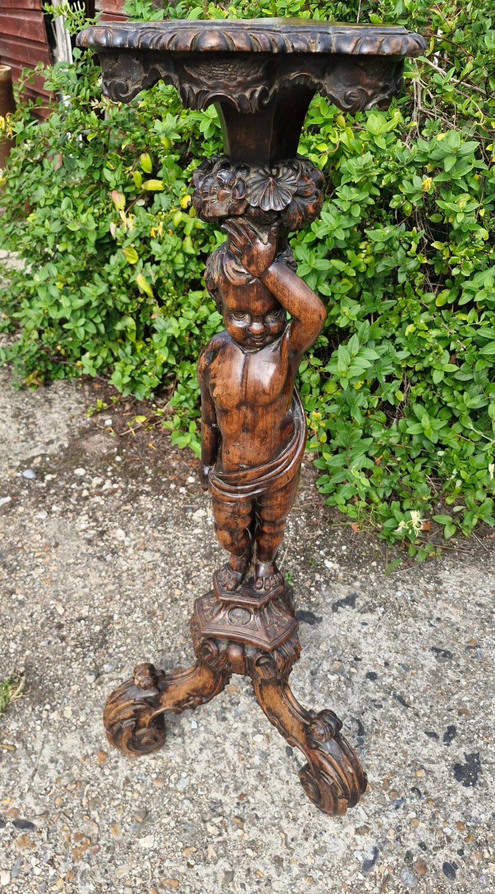 A 19th-century Italian dark carved wood pedestal stand with a putto figure support, scalloped top, and scroll tripod feet. View III