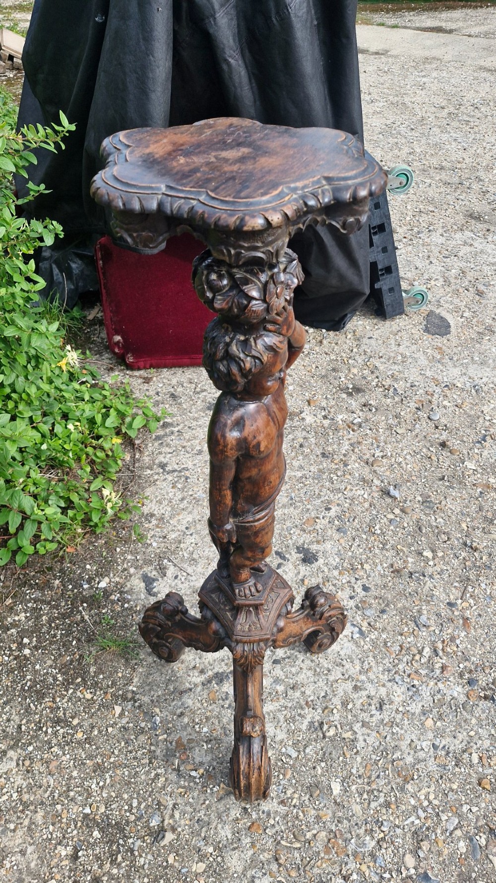 A 19th-century Italian dark carved wood pedestal stand with a putto figure support, scalloped top, and scroll tripod feet. View IV