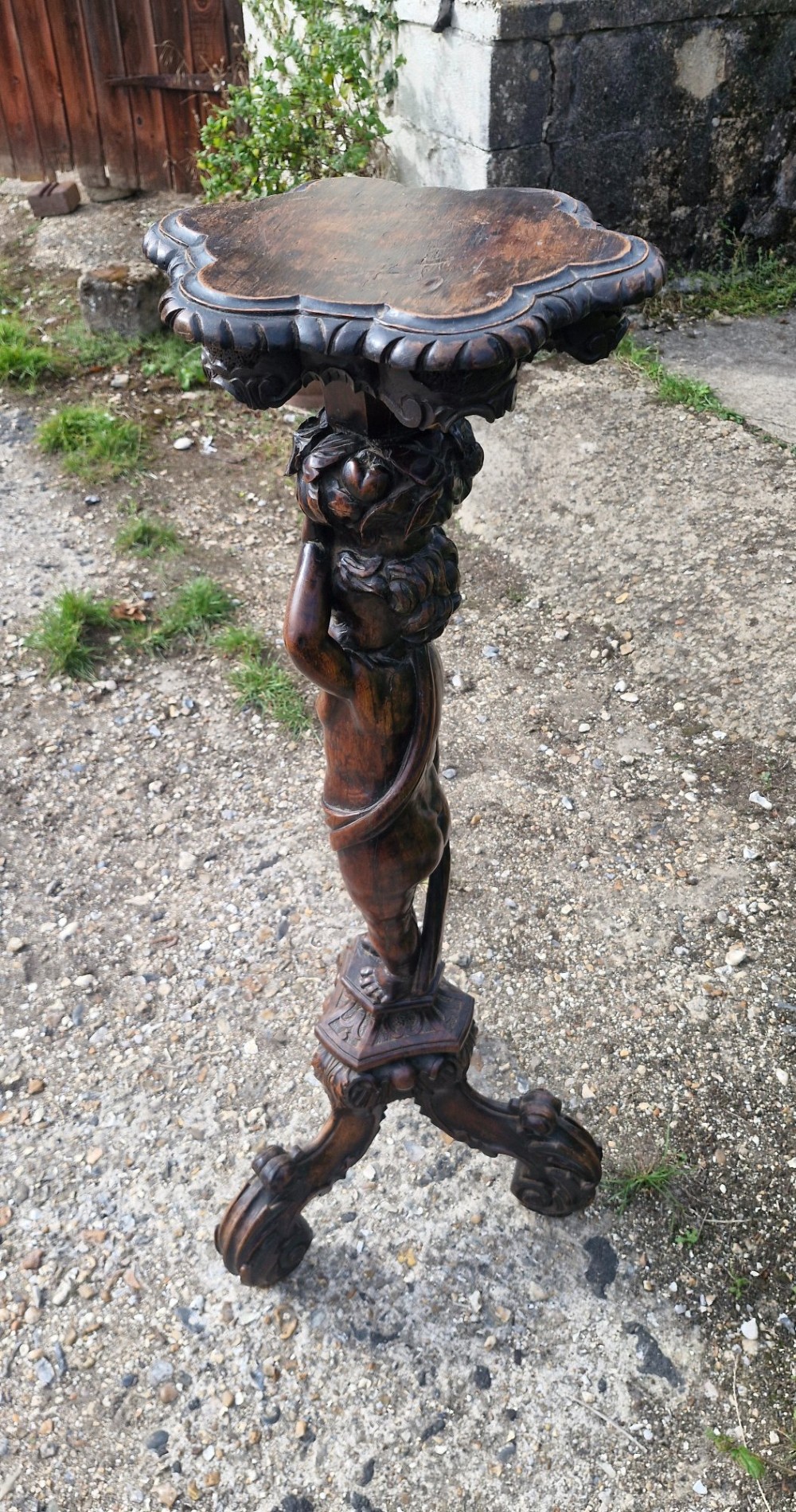 A 19th-century Italian dark carved wood pedestal stand with a putto figure support, scalloped top, and scroll tripod feet. View V