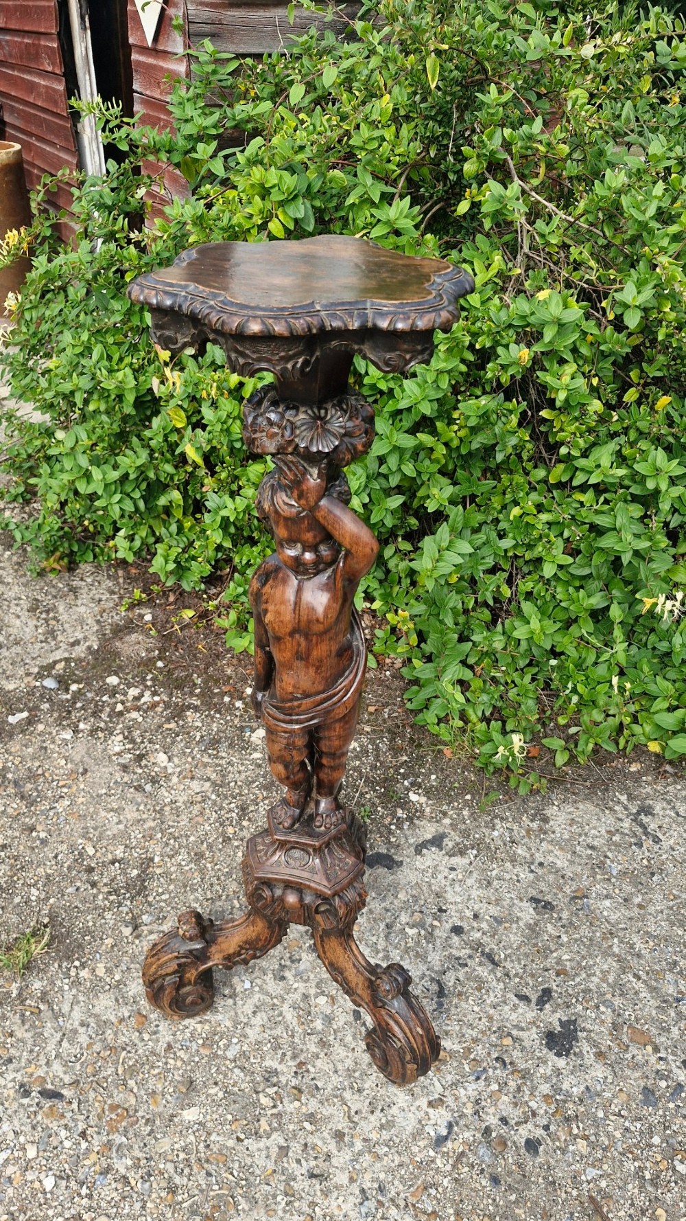 A 19th-century Italian dark carved wood pedestal stand with a putto figure support, scalloped top, and scroll tripod feet. View VI