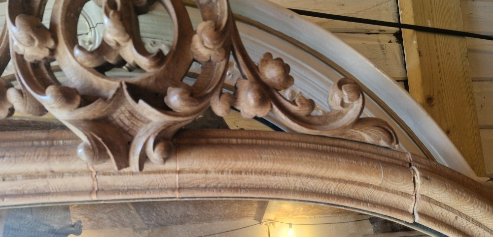 A large 19th-century arched oak wall mirror featuring an intricate carved scrollwork crest and a molded frame. View VI