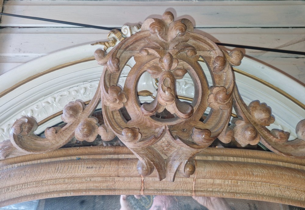 A large 19th-century arched oak wall mirror featuring an intricate carved scrollwork crest and a molded frame. View VIII