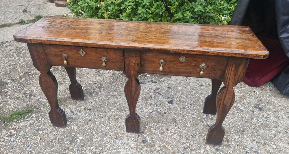 An early 19th-century country oak serving table featuring a long rectangular top, two drawers with brass teardrop handles, and shaped flat-profile legs. View V