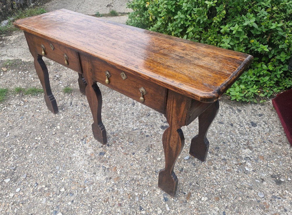 An early 19th-century country oak serving table featuring a long rectangular top, two drawers with brass teardrop handles, and shaped flat-profile legs. View VI