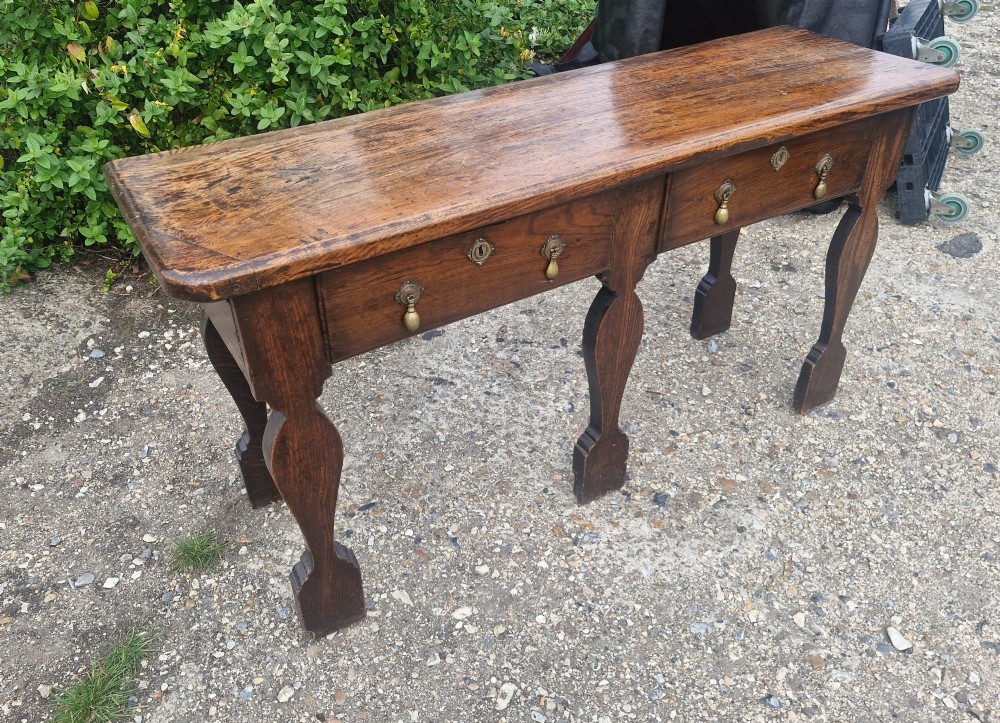An early 19th-century country oak serving table featuring a long rectangular top, two drawers with brass teardrop handles, and shaped flat-profile legs. View VII