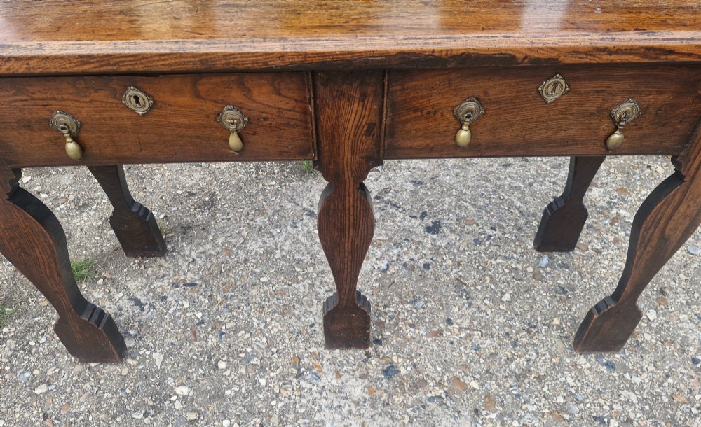 An early 19th-century country oak serving table featuring a long rectangular top, two drawers with brass teardrop handles, and shaped flat-profile legs. View VIII