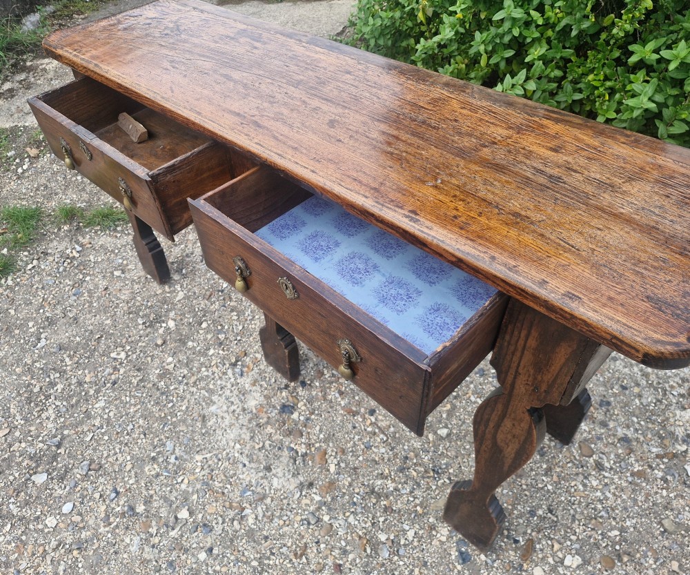 An early 19th-century country oak serving table featuring a long rectangular top, two drawers with brass teardrop handles, and shaped flat-profile legs. View IX