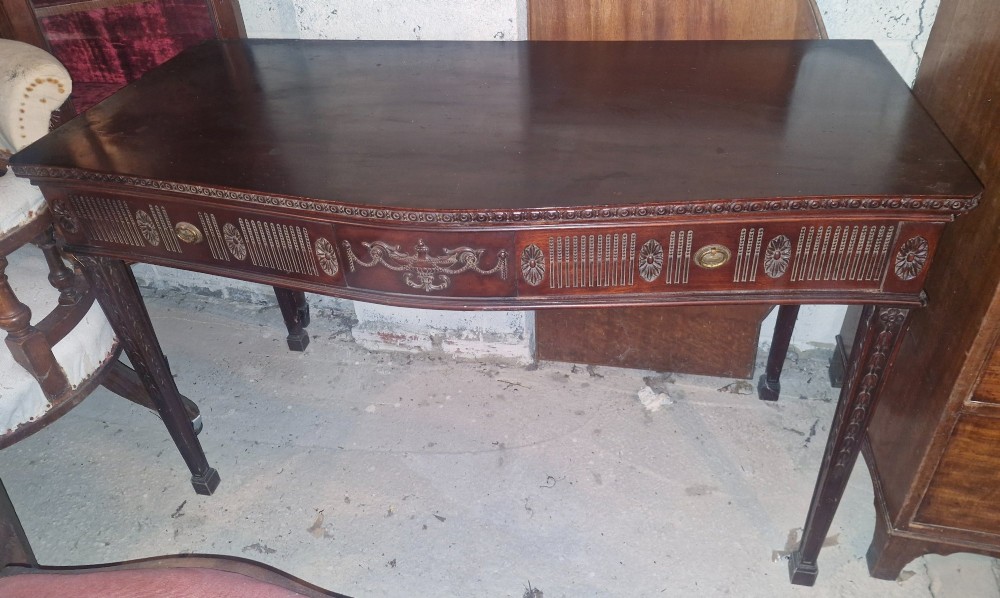 An Edwardian dark mahogany serving table featuring a shaped bow front, carved swags and fluted frieze decoration, two drawers, and square tapered legs. View III