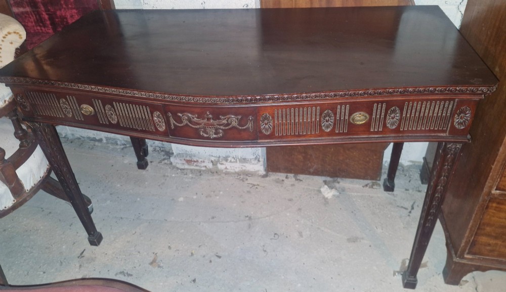 An Edwardian dark mahogany serving table featuring a shaped bow front, carved swags and fluted frieze decoration, two drawers, and square tapered legs. View IV