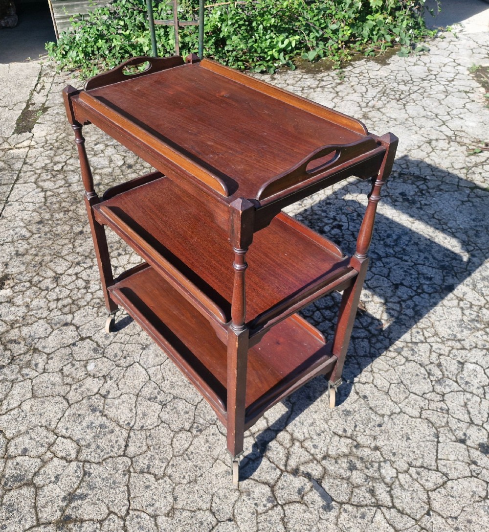 A three-tier dark mahogany wooden tea trolley featuring turned corner posts, castor wheels, and a top removable tray with cut-out handles. View II