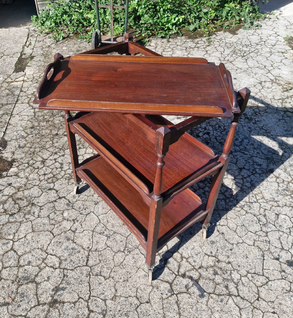 A three-tier dark mahogany wooden tea trolley featuring turned corner posts, castor wheels, and a top removable tray with cut-out handles. View III