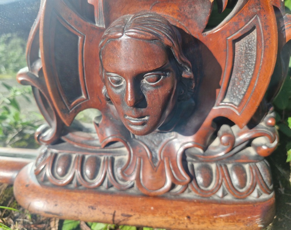 An antique Victorian carved mahogany overmantel mirror featuring an arched frame decorated with carved human faces, scrollwork, and foliate details. View II