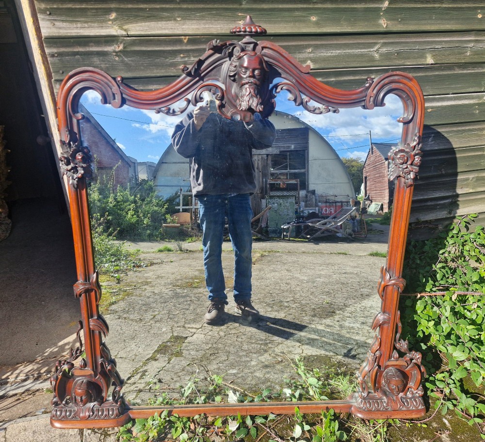 An antique Victorian carved mahogany overmantel mirror featuring an arched frame decorated with carved human faces, scrollwork, and foliate details. View VII