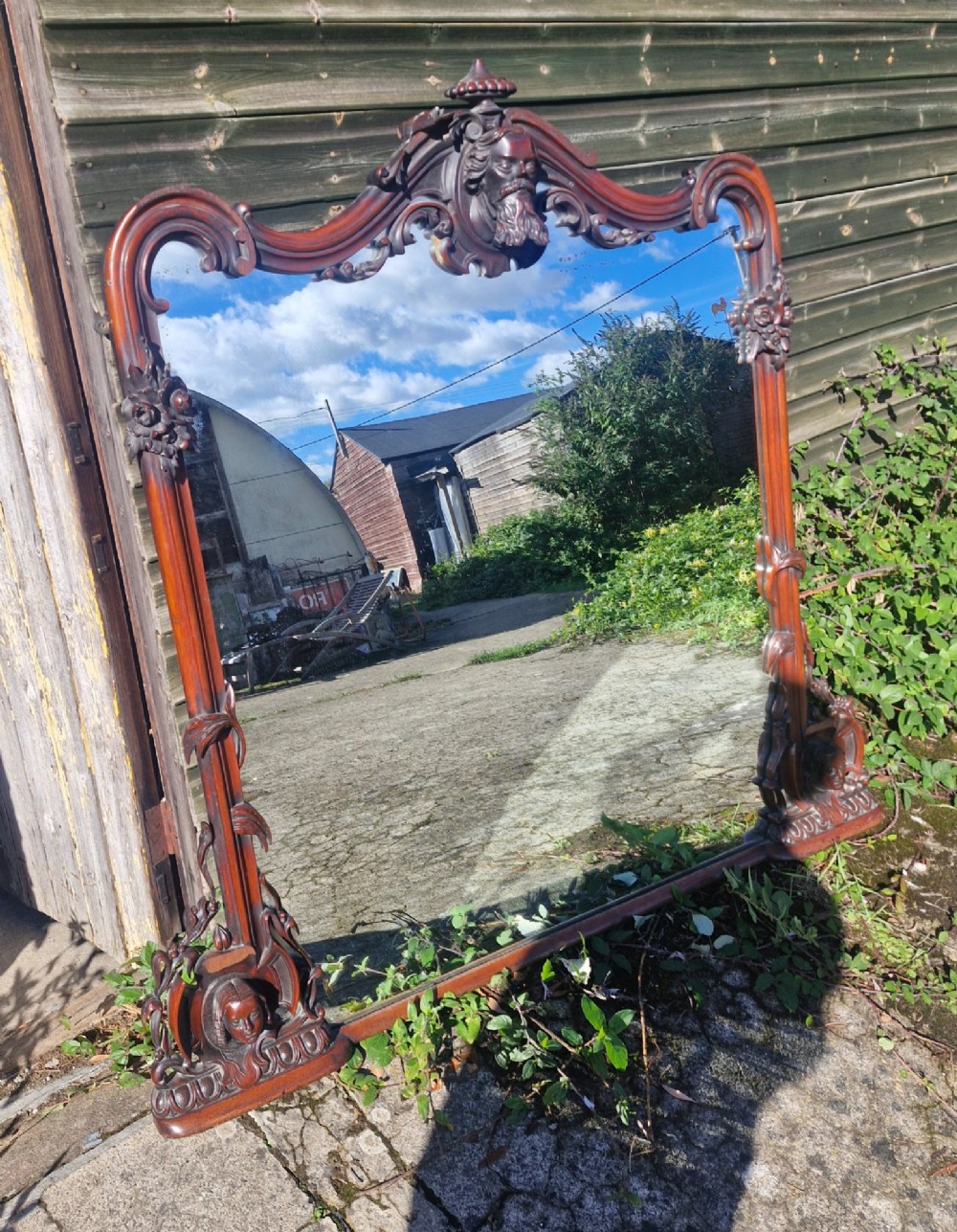 An antique Victorian carved mahogany overmantel mirror featuring an arched frame decorated with carved human faces, scrollwork, and foliate details. View VIII