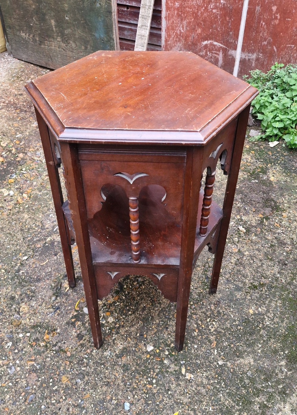 A dark mahogany hexagonal occasional table featuring a lower shelf, turned spindle supports, and cut-out decorative aprons.