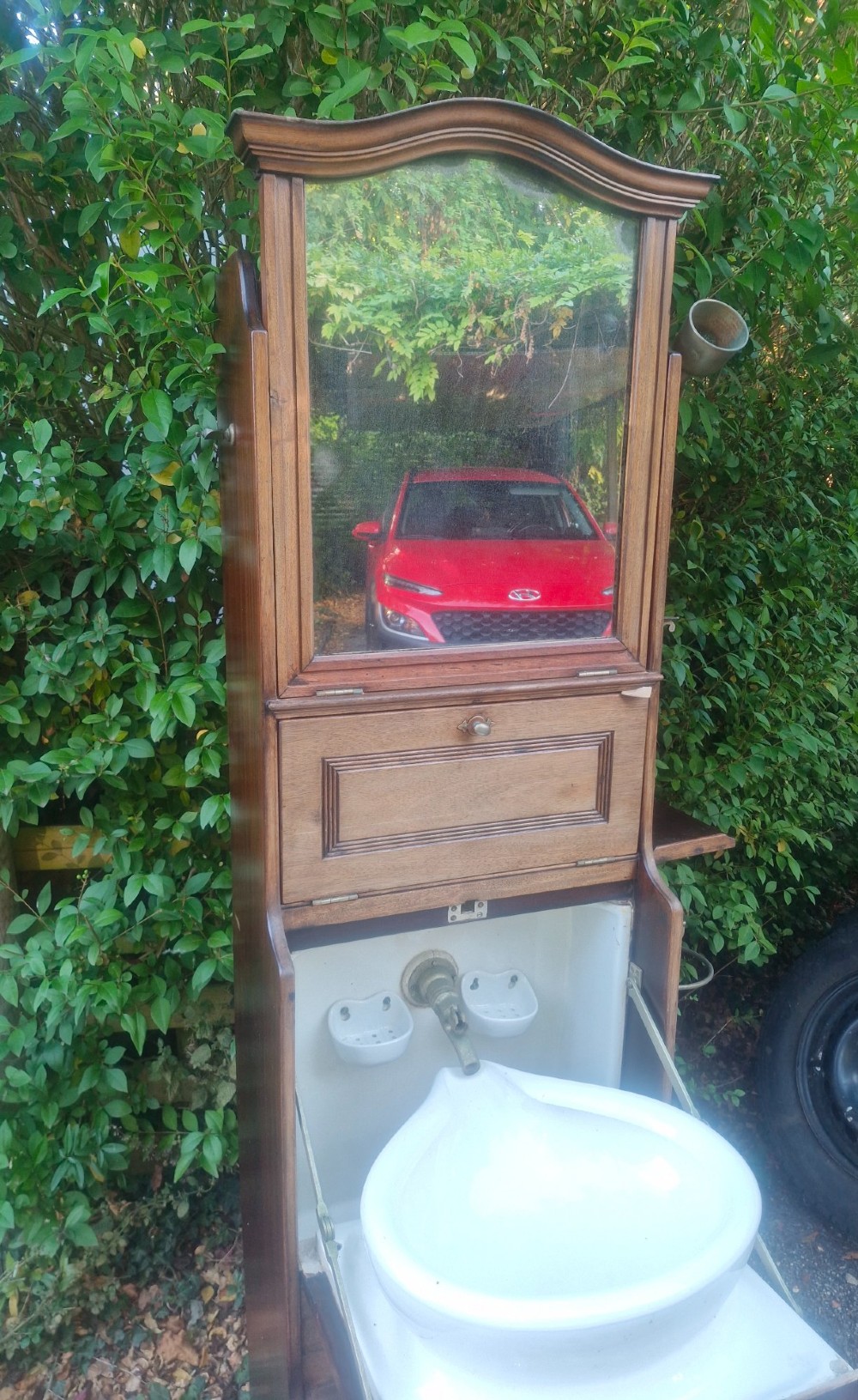 An Edwardian wooden ships washstand featuring an upper arched mirror, a middle drop-front door revealing a white ceramic washbasin, and lower cupboard doors. View II