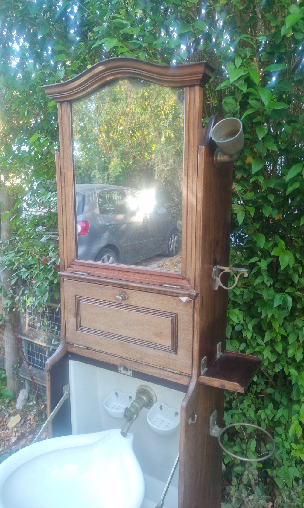 An Edwardian wooden ships washstand featuring an upper arched mirror, a middle drop-front door revealing a white ceramic washbasin, and lower cupboard doors. View III