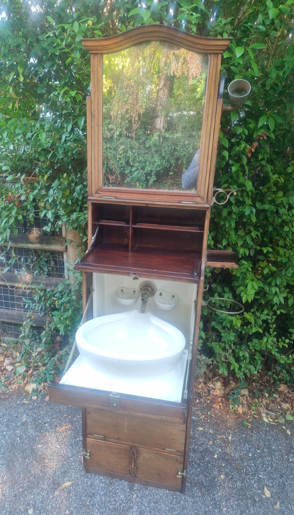 An Edwardian wooden ships washstand featuring an upper arched mirror, a middle drop-front door revealing a white ceramic washbasin, and lower cupboard doors. View VII