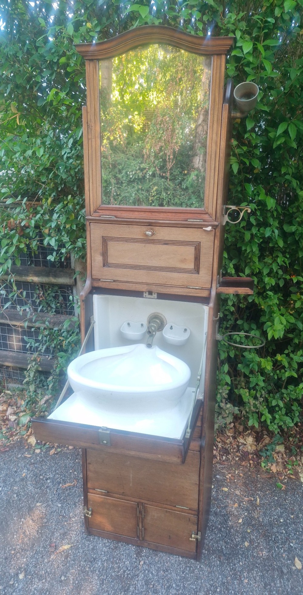 An Edwardian wooden ships washstand featuring an upper arched mirror, a middle drop-front door revealing a white ceramic washbasin, and lower cupboard doors. View XV