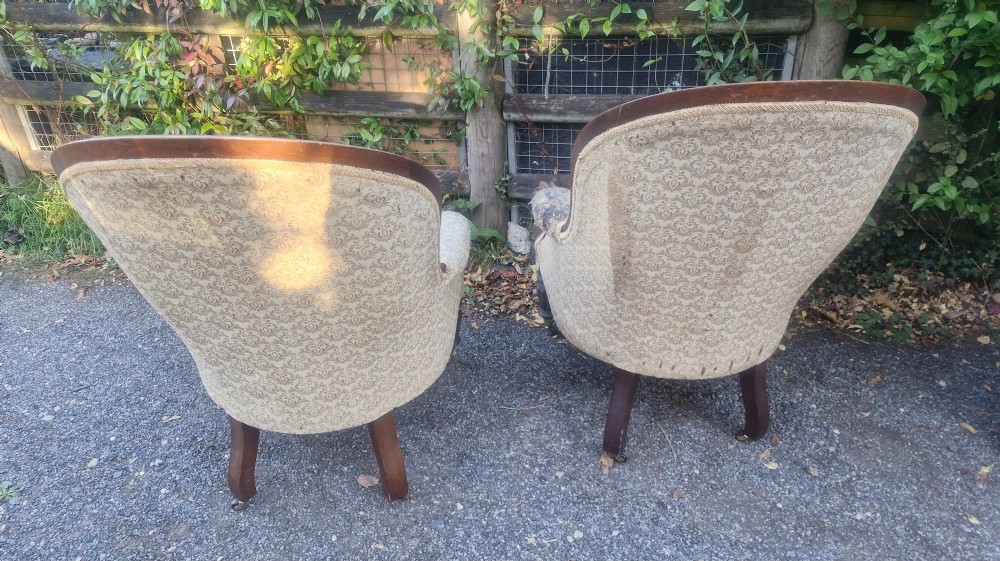 A pair of Victorian mahogany library armchairs featuring deep button-back patterned upholstery, carved scroll arms, and turned legs with brass castors. View II