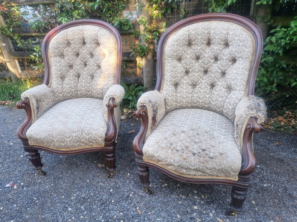 A pair of Victorian mahogany library armchairs featuring deep button-back patterned upholstery, carved scroll arms, and turned legs with brass castors. View III