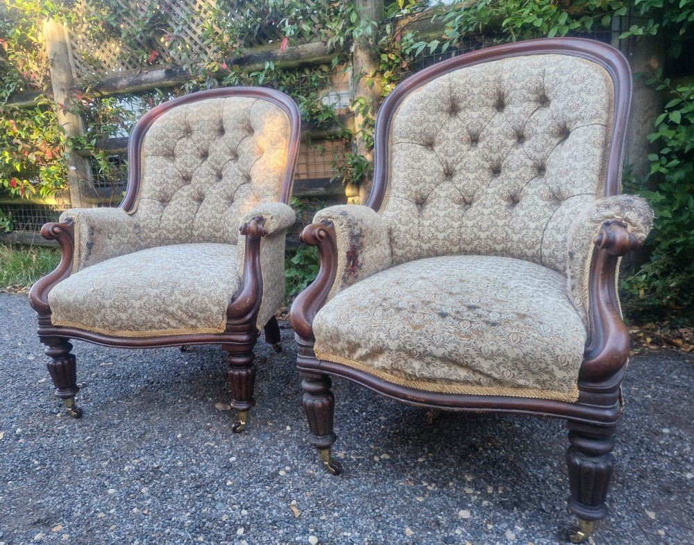 A pair of Victorian mahogany library armchairs featuring deep button-back patterned upholstery, carved scroll arms, and turned legs with brass castors. View IV