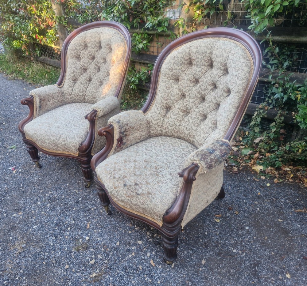 A pair of Victorian mahogany library armchairs featuring deep button-back patterned upholstery, carved scroll arms, and turned legs with brass castors. View V