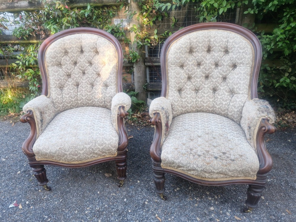 A pair of Victorian mahogany library armchairs featuring deep button-back patterned upholstery, carved scroll arms, and turned legs with brass castors. View VII
