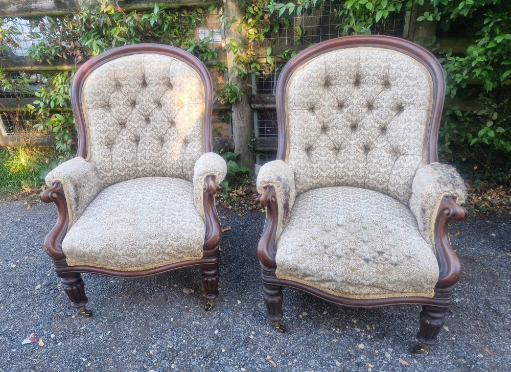 A pair of Victorian mahogany library armchairs featuring deep button-back patterned upholstery, carved scroll arms, and turned legs with brass castors. View VIII